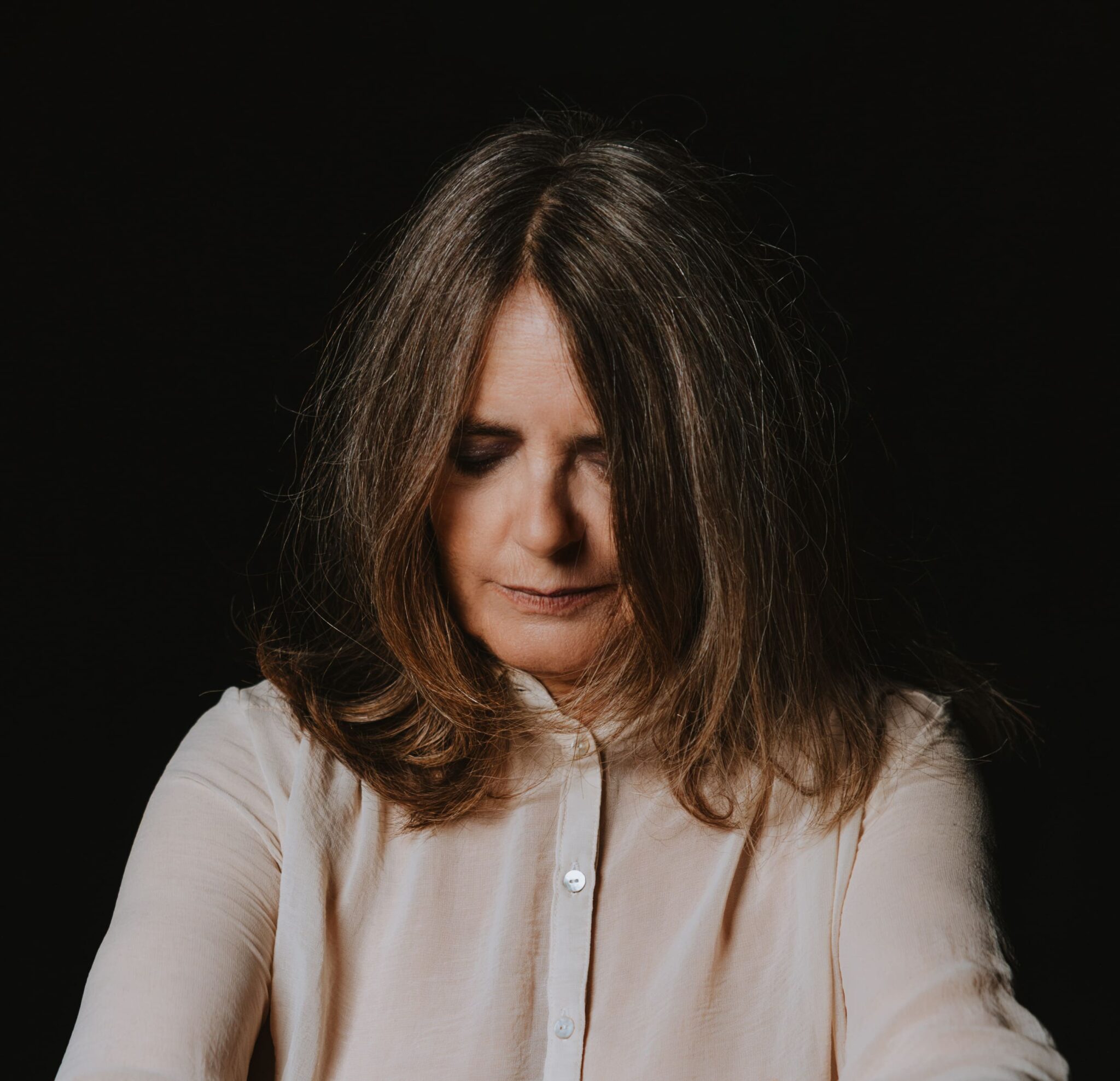 Foto della cantante Nada, capelli lisci sulle spalle, sguardo basso, sfondo nero