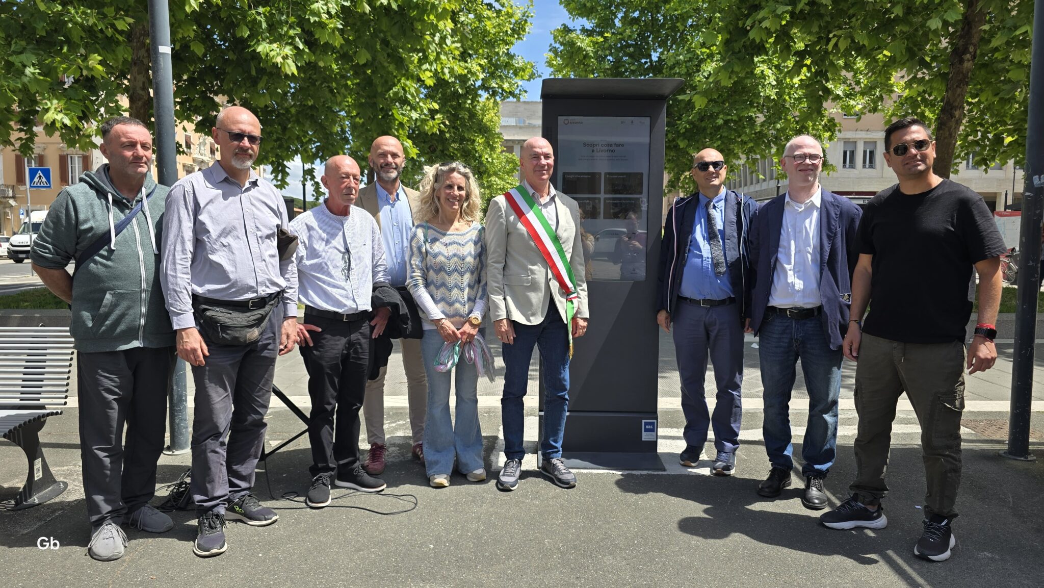 Foto di gruppo davanti al totem ancora coperto da drappo amaranto
